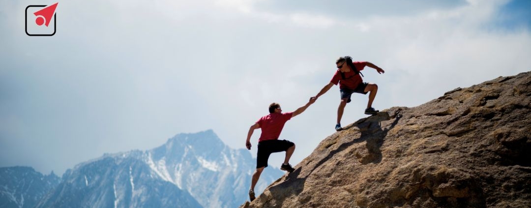 Hombre ayuda a otro a escalar a la cima de la montaña