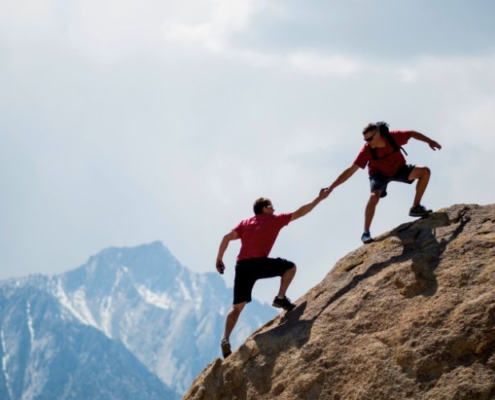 Hombre ayuda a otro a escalar a la cima de la montaña